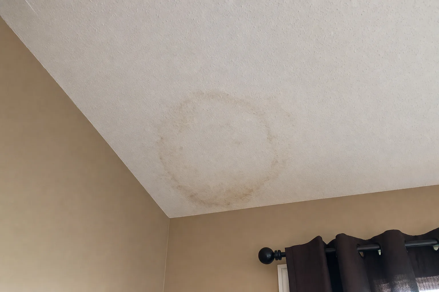 Bedroom ceiling corner with a faint brownish water stain ring and light mottled discoloration from past moisture.
